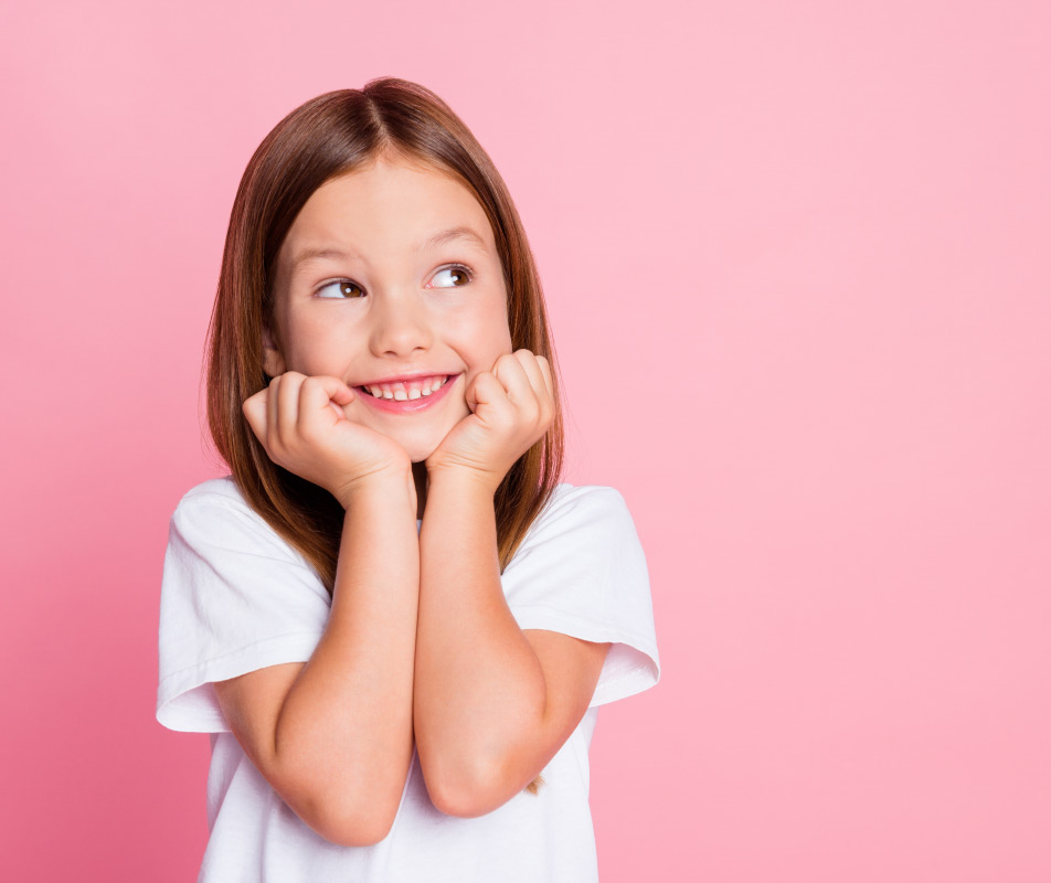 Happy child smiling with hands on face against pink background, pediatric dental care concept.