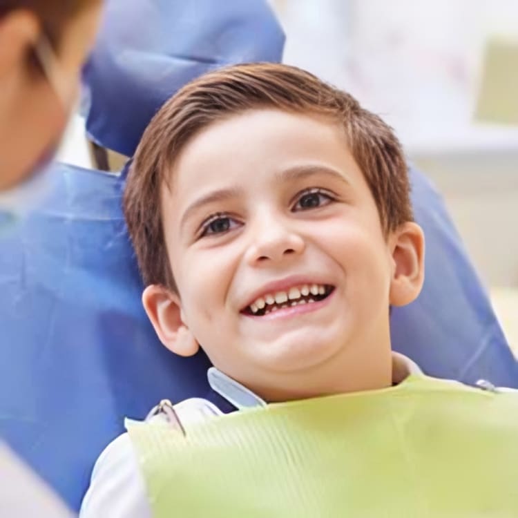 Smiling young boy sitting in a dental chair during a checkup at a pediatric dentist’s office.