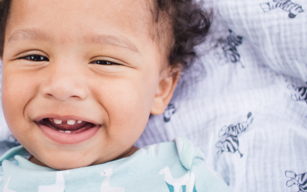 Smiling Baby Showing First Teeth – When to Start Brushing A smiling baby with first teeth visible, representing the stage when parents should begin brushing their child’s teeth.