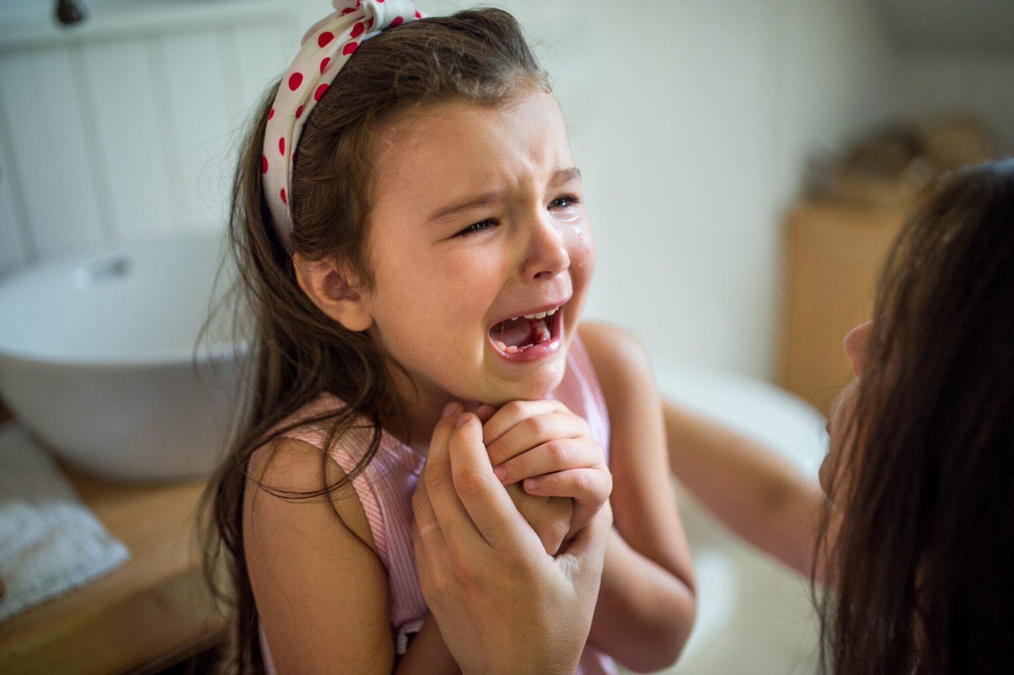 Upset young girl clutching her jaw while an adult comforts her, suggesting tooth pain or a dental emergency