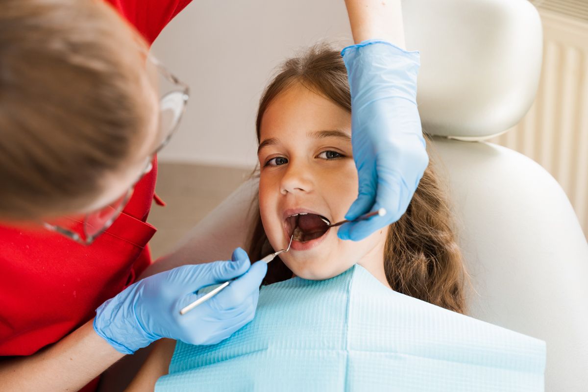 A pediatric dentist examining a child’s teeth during a dental visit, highlighting early detection and treatment of cavities with fillings.