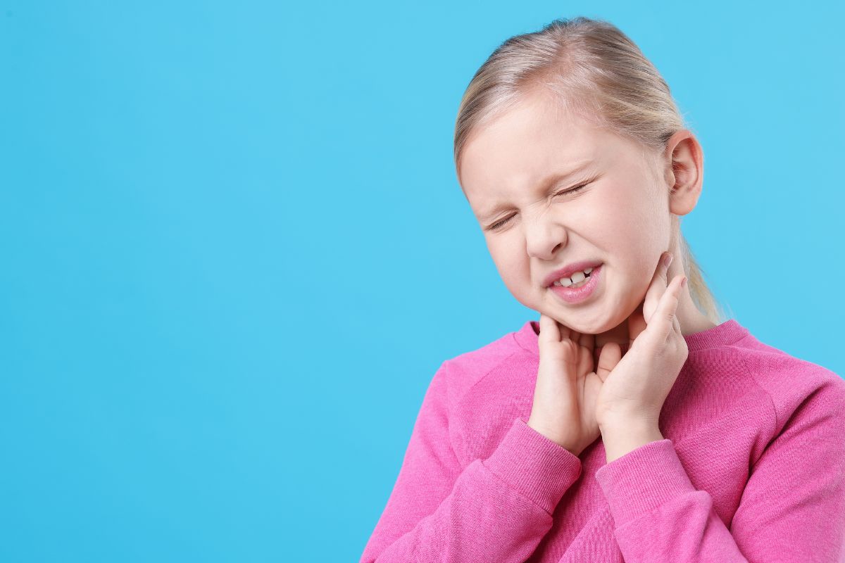 A young girl holds her jaw and neck in discomfort, highlighting facial swelling or pain that should not be ignored.