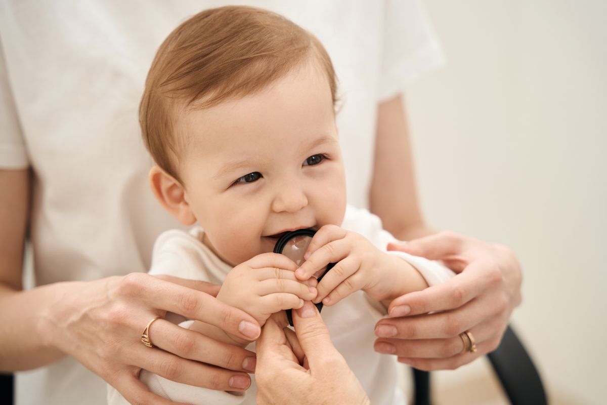 A smiling baby chews on a teething toy while being comforted by a caregiver during the teething stage.