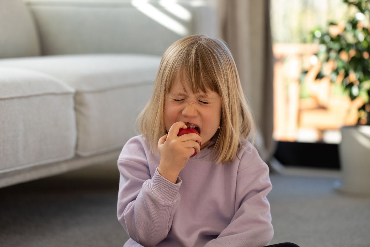 Early Warning Signs of Jaw Problems in Children include pain while chewing, shown by a young child experiencing tooth or jaw discomfort while eating fruit, highlighting the need for prompt pediatric dental evaluation.